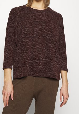 Maglione a maglia color bordeaux con un motivo testurizzato, colletto rotondo e maniche a 3/4, abbinato a pantaloni marroni a coste. Taglio semplice e rilassato.
