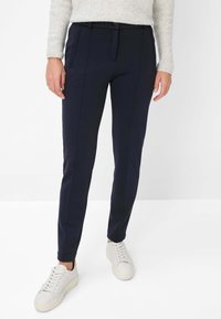 Marineblaue, schmal zulaufende Hose mit glatter Textur, seitlichen Taschen, Knopfverschluss und taillierter Passform, kombiniert mit weißen Sneakers.