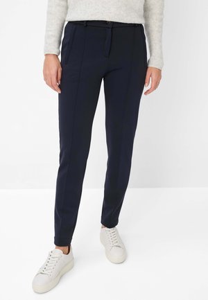 Navy tapered trousers with a smooth texture, featuring side pockets, a button closure, and a tailored fit, paired with white sneakers.