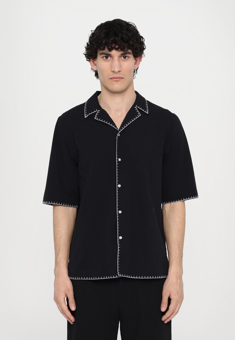 Black short-sleeve shirt with white contrasting stitching along the collar and cuffs, featuring a button-down front. Smooth fabric texture.