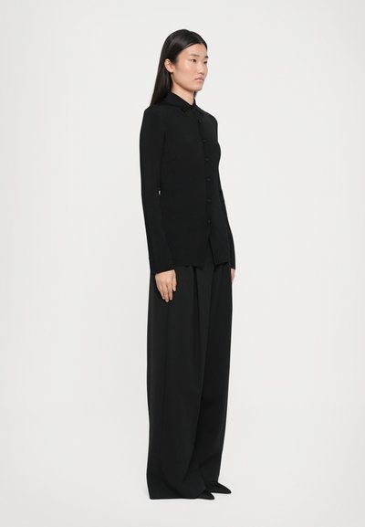 Camicia nera attillata con colletto, abbinata a pantaloni neri a gamba larga. Tessuto liscio, design minimale, senza motivi o dettagli visibili.