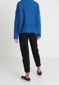 Pull bleu en tricot avec un motif texturé, associé à un pantalon noir fuselé et des baskets en toile noires. Le pull a une coupe décontractée.