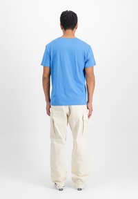 Modrá bavlněná tričko s kulatým výstřihem, spárované s krémovými cargo kalhotami. Kalhoty mají velké boční kapsy a volný střih.