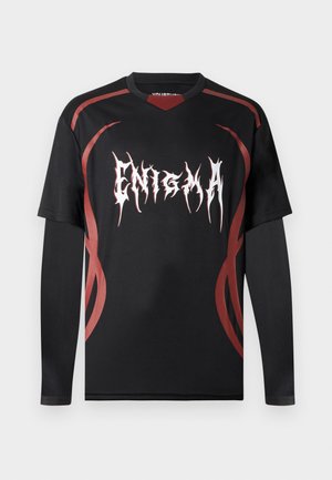Μαύρο μακρυμάνικο στρωματοποιημένο πουκάμισο με κόκκινα αφηρημένα σχέδια που μοιάζουν με φλόγες και έντονο λευκό κείμενο "ENIGMA" σε στιλιζαρισμένη γραμματοσειρά στο στήθος.
