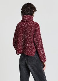 Gestrickter bordeauxfarbener Pullover mit hohem Kragen, strukturiertem Muster und cropped Schnitt, kombiniert mit dunklen Jeans aus Denim mit zwei Gesäßtaschen.