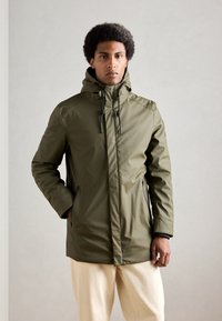 Oliven grøn vandtæt parka med en høj krave, justerbar hætte og lynlåslommer i siden. Glat tekstur og strømlinet design.