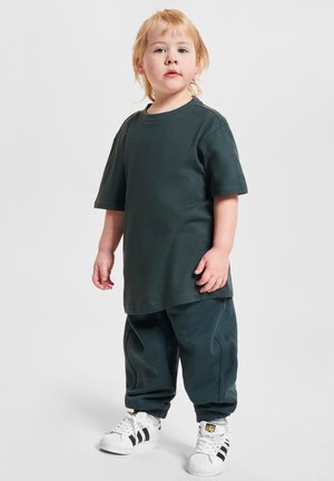 T-shirt en coton vert foncé et pantalon de survêtement assorti avec des poignets côtelés. Baskets blanches avec des rayures noires sur les côtés. Design simple et coupe décontractée.