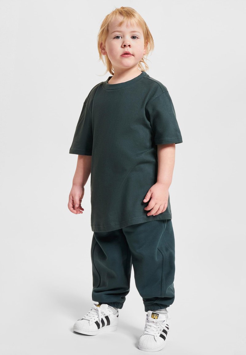 Dunkelgrünes Baumwoll-T-Shirt und passende Sweatpants mit gerippten Bündchen. Weiße Sneaker mit schwarzen Streifen an den Seiten. Einfaches Design und lässige Passform.