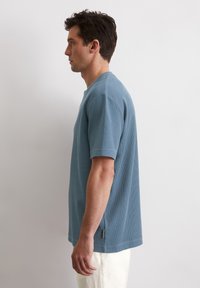 Korte mouwen, ronde hals t-shirt in lichtblauwe textuurstof met een relaxte pasvorm. Heeft subtiele brandingdetails in de zijnaad.