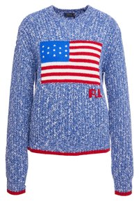 Pull en tricot bleu avec un motif de drapeau américain bien en vue en rouge, blanc et bleu, doté d'un ourlet inférieur rouge et d'un logo brodé.