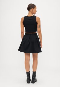 Crni crop top i kombinacija sa suknjom koja se širi. Top ima prilagođeni dizajn, a suknja s plisirima. Upari s crnim čizmama do gležnja.