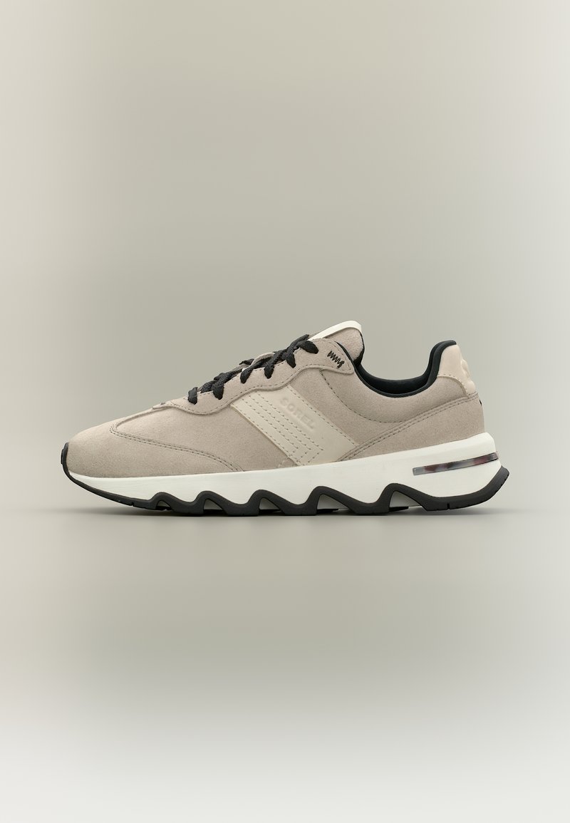 Μπεζ σουέντ αθλητικό παπούτσι με μαύρα κορδόνια, λευκή ενδιάμεση σόλα και μαύρη εξωτερική σόλα με κυματιστό σχέδιο, εμφανισμένο σε πλευρικό προφίλ σε ουδέτερο φόντο.