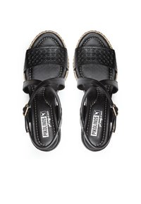 Sandales en cuir noir avec des bandes tissées, une large sangle à l'avant et une sangle à la cheville. Présente une surface texturée et des coutures de couleur claire.