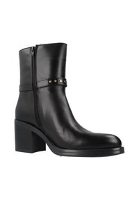 Botín de cuero negro hasta el tobillo con cremallera lateral, tacón cuadrado y correa decorativa con clavos metálicos. Textura suave y puntera redondeada.