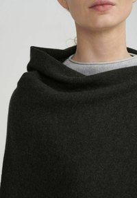 Châle en laine gris foncé avec un design drapé. Il présente une texture douce et un décolleté ouvert, superposé à un haut en tricot gris clair.