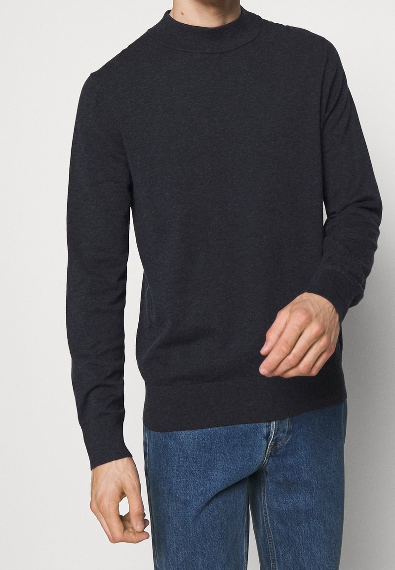 Dunkelgrauer Langarmpullover mit hohem Kragen, gerippten Bündchen und Saum, aus einem weichen, strukturierten Material, kombiniert mit blauen Jeans.
