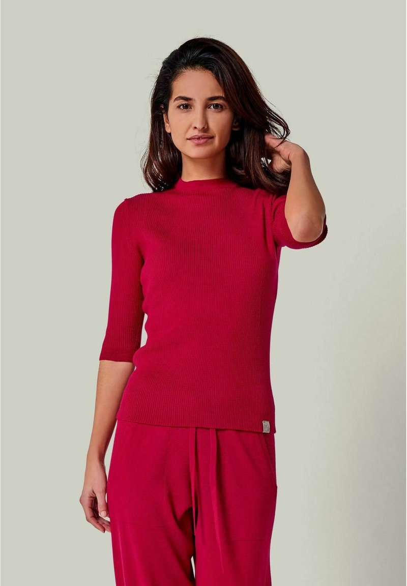 Rotes geripptes Strickoberteil mit kurzen Ärmeln und hohem Ausschnitt, das am Saum ein kleines Logo-Detail und eine enganliegende Passform hat.