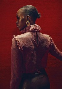 Blusa de encaje en color malva con cuello volante y abertura en la espalda, combinada con pantalones de cuero negros. Pendientes llamativos en dorado y burdeos.