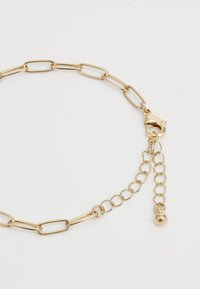 Bracelete de ouro com elos de corrente mistos e fecho tipo lagosta, apresentando uma corrente de extensão ajustável que termina com um pequeno encantamento em forma de bola de ouro.