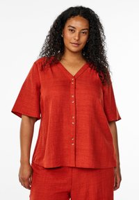 Blusa rossa a maniche corte con scollatura a V e chiusura a bottoni, realizzata in un tessuto testurizzato. Vestibilitàampia con orlo dritto.