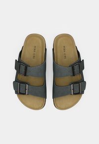 Černé skluzné sandály s dvěma nastavitelnými přezkami, vyrobené z měkkého materiálu, s texturovanou stélkou a světle hnědou vložkou.