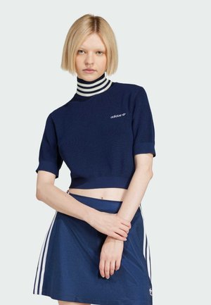 Navy cropped sweater with short sleeves and ribbed high collar, featuring white stripes and embroidered Adidas logo. Worn with a matching skirt.