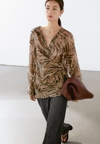 Bluse med brune og sorte tigerstriber, lange ærmer, dyb V-udskæring, parret med mørk denimbukser og en vævet burgunder clutch.
