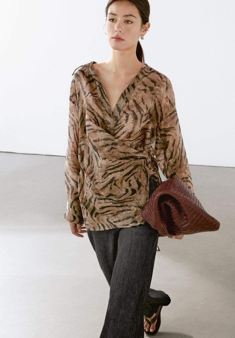 Bluse med brune og sorte tigerstriber, lange ærmer, dyb V-udskæring, parret med mørk denimbukser og en vævet burgunder clutch.