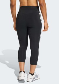 Crne capri tajice s visokim pojasom i bijelim bočnim prugama. Glatke teksture; uparen s bijelim i sivim sportskim cipelama.