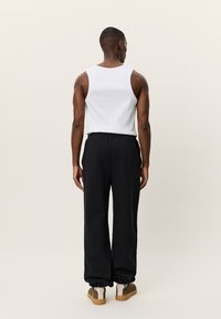 Λευκή αμάνικη μπλούζα τύπου τοπ συνδυασμένη με μαύρο παντελόνι, με ελαστικές μανσέτες και κορδόνι στη μέση. Φορεμένη με καφέ και κρεμ αθλητικά παπούτσια.