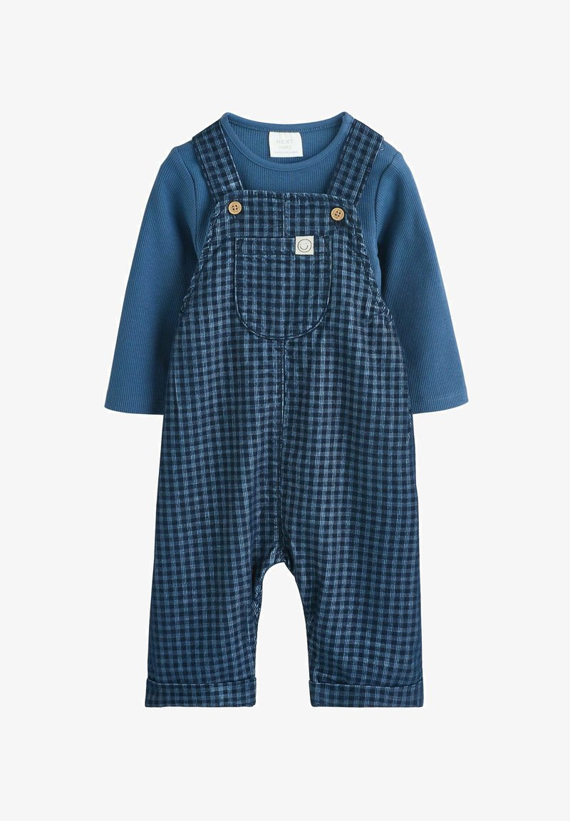 Marineblauwe geblokte tuinbroek met houten knoopaccenten, gecombineerd met een blauwe ribgebreide langemouwshirt eronder.