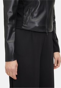 Czarna skórzana kurtka o gładkiej fakturze, z kieszenią na zamek i dopasowanym krojem, w zestawie z czarnymi materiałowymi spodniami.