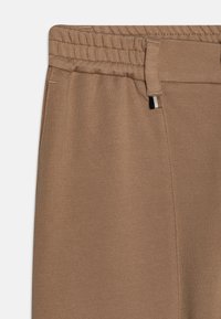 Joggers marroni con vita elastica realizzati in morbido tessuto, caratterizzati da una texture liscia, cuciture sottili e un piccolo dettaglio con etichetta nera e bianca.