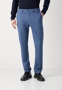 Modré chinos vyrobené z lehkého materiálu, se střihovým designem s rovnými nohavicemi a zapínáním na knoflík, v kombinaci s černými šněrovacími botami.