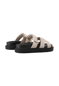 Sandali in tessuto beige con quattro cinghie incrociate, suola in gomma nera, design piatto e superficie testurizzata per la presa. Stile minimalista e versatile.