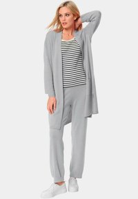 Lichtgrijze lange cardigan over een gestreept shirt en bijpassende broek, gecombineerd met witte sneakers. Zachte, comfortabele stof met een relaxte pasvorm.