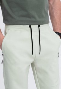 Lichtgroene joggingbroek met een koord in de taille, zwarte trekkoorden, zijzakken met rits en een gladde, textuurstof.