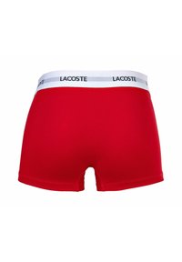 Boxer a vita bassa rossi con elastico bianco recante il logo "LACOSTE". Il tessuto appare liscio e elasticizzato, progettato per garantire comfort.
