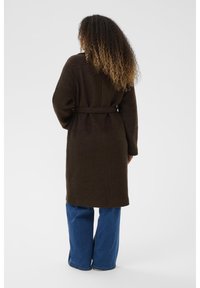 Bruine wolmix jas met een ceintuur in de taille, ronde halslijn en lange mouwen, gecombineerd met wijdvallende blauwe spijkerbroeken.