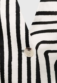 Black and white striped fabric featuring varying thick and thin lines. A round, light-colored button is attached near the neckline.