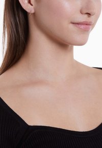 Boucles d'oreilles en or, en forme de créoles avec un design texturé et torsadé, portées dans une oreille percée. La teinte de la peau est claire avec une apparence lisse et naturelle.