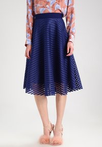 Marinblå plisserad kjol med en strukturerad, lager-på-lager design. Längd till mitten av vadderna med ett brett midjeband och subtila mönster i utklipp.