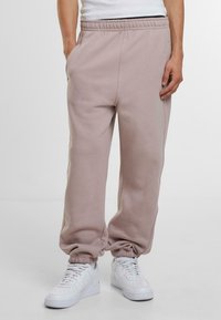 Pantaloni de trening roz deschis cu talie elastică și mansete. Au buzunare laterale și o textură netedă, moale. Asortați cu adidași albi.