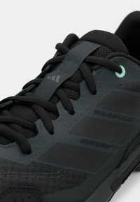 Black athletic shoe with textured mesh upper, rubber outsole, and three dark stripes. Features tonal laces and mint accent on the eyelet.