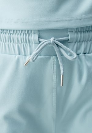 Pantalones jogger azul claro con cintura elástica y cordón. Textura suave con puntas metálicas plateadas en el cordón.