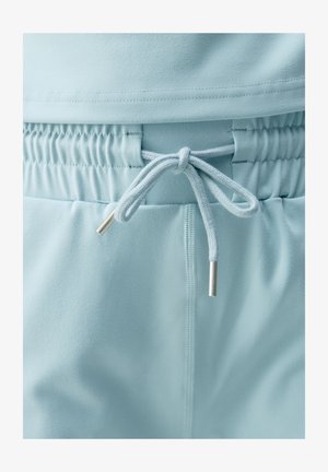 Jasnoniebieskie spodnie dresowe z elastycznym pasem i sznurkiem do regulacji. Gładka faktura z metalowymi końcówkami w kolorze srebrnym na sznurku.
