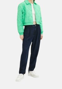 Zielona pikowana krótka kurtka, biała bluzka, ciemnoniebieskie luźne dżinsy i białe trampki. Kurtka ma zapięcie na guziki oraz elastyczne mankiety.