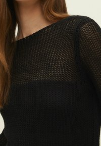 Pull noir en maille présentant un motif lâche et texturé, avec un col rond et des manches longues, mettant en valeur un tissu doux et respirant.