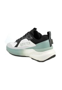Sneaker bianca e nera con tomaia testurizzata, marchio GORE-TEX, accento verde chiaro sul tallone e una suola intermedia bianca chunky.