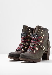 Par de botas de cuero marrón oscuro hasta el tobillo con tacones apilados, cordones burdeos, lengua de punto y correas decorativas con hebillas en tono dorado.